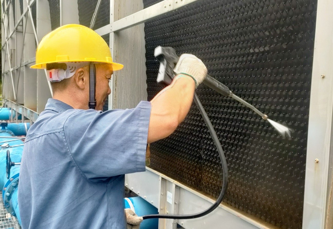 Teknisi membersihkan fill cooling tower dengan alat bertekanan